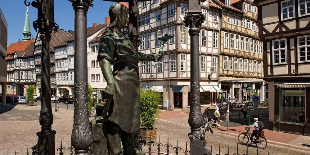 Blick auf einen Brunnen mit Figur und schmiedeeiserner Figur, dahinter Fachwerkhäuser